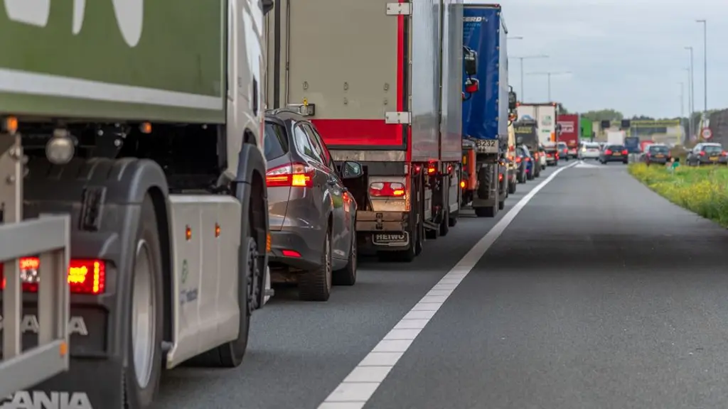 Zijaanzicht vanaf de zijkant van een snelweg waar een lange rij vrachtwagens en personenauto's achter elkaar stilstaat in een file.